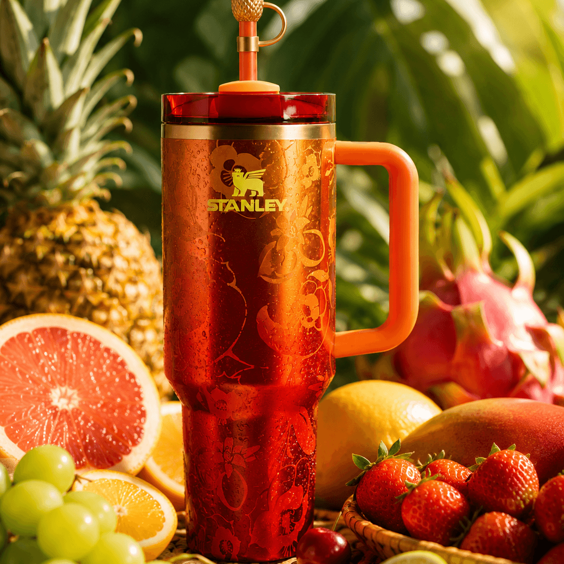 Red Stanley mug with handle surrounded by fruits on a green leafy background