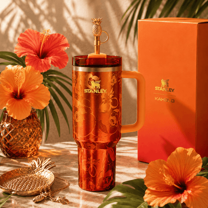 Orange Stanley mug with pineapple design on a decorative table with flowers and packaging.
